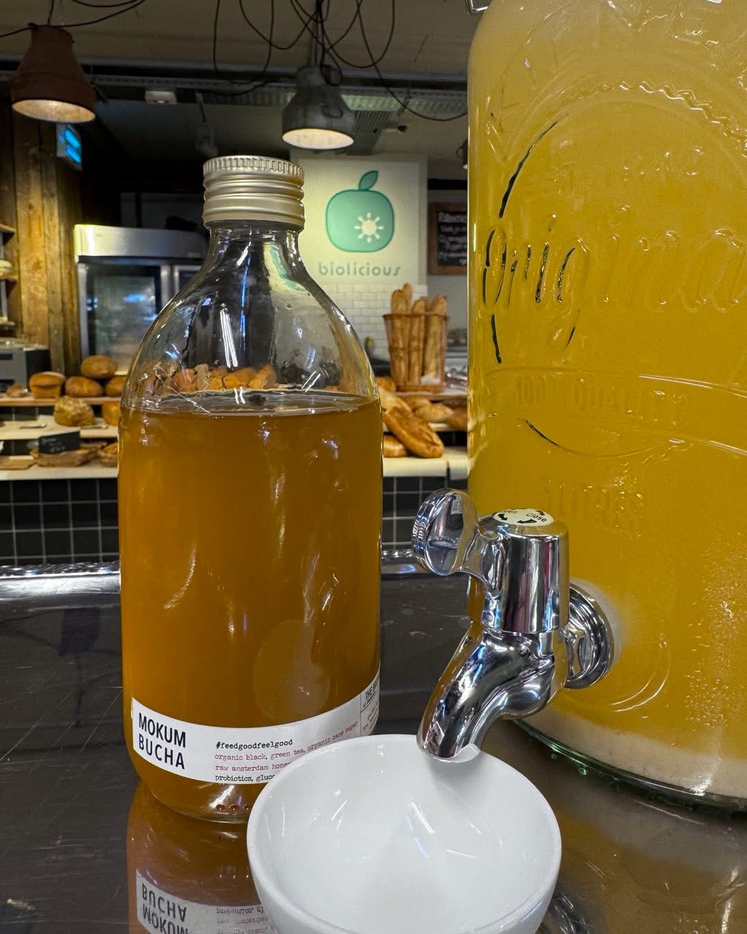 Kombucha bij Biolicious, met de broodbalie en het winkellogo op de achtergrond